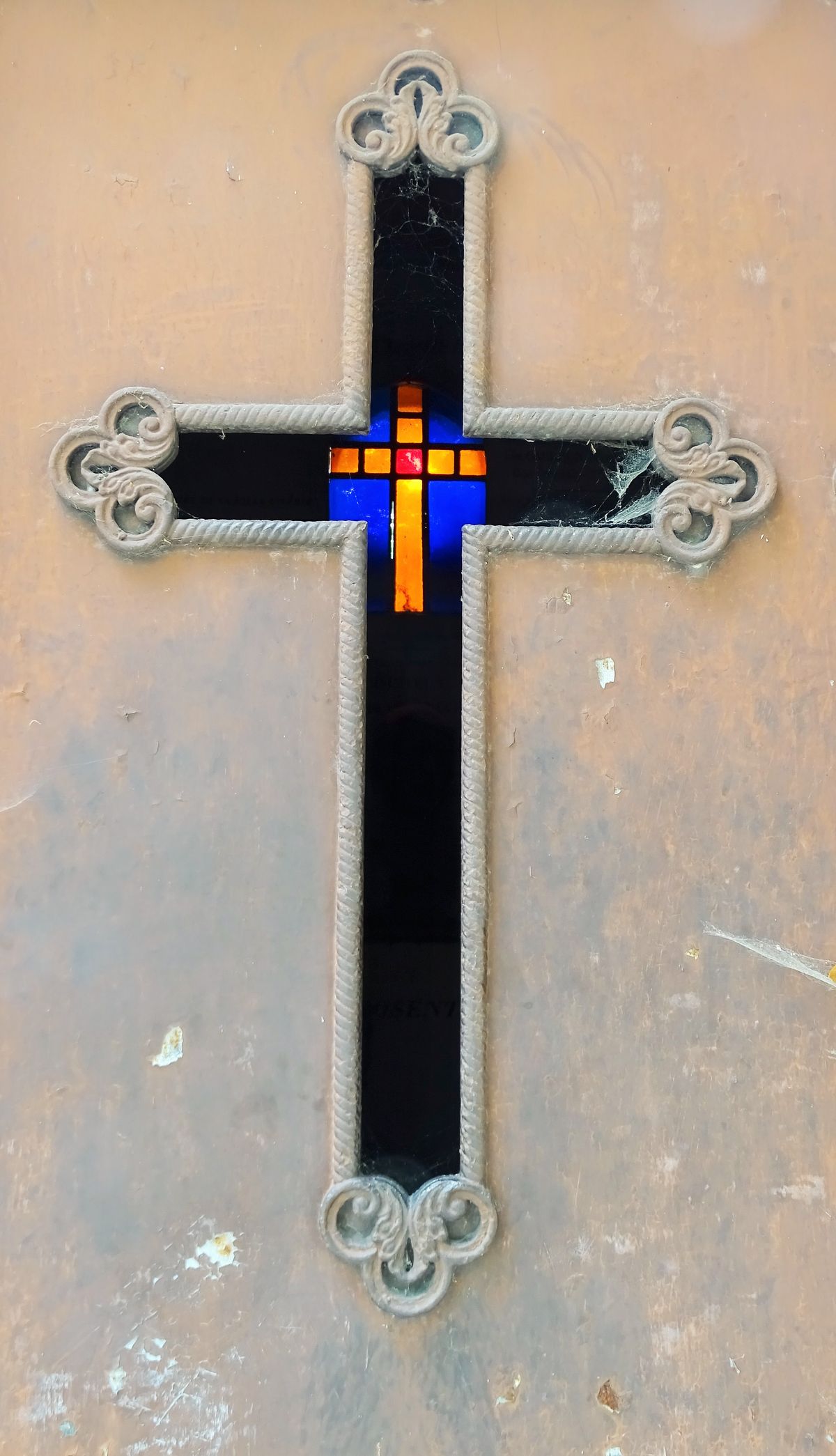 cross on the door of a vault with a stained glass window at the bottom
